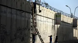 Pemuda Palestina berusaha memanjat tembok pembatas Israel saat berangkat untuk beribadah salat Jumat di Masjid Al-Aqsa, Yerusalem, Jumat (9/6). Para pemuda ini nekat memanjat untuk menghindari pengawasan tentara Israel. (AFP Photo/Abbas Momani)