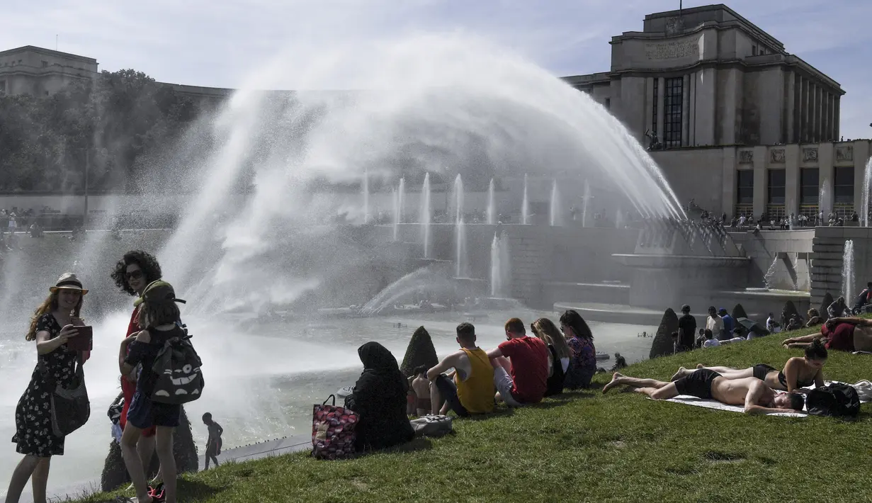 Sejumlah warga duduk dirumput di dekat air mancur di Trocadero Fountains dekat Menara Eiffel, Paris (22/7/2019). Warga Paris bersiap menghadapi suhu terpanas pada minggu ini ketika gelombang panas akan melanda ke Eropa utara. (AFP Photo/Alain Jocard)