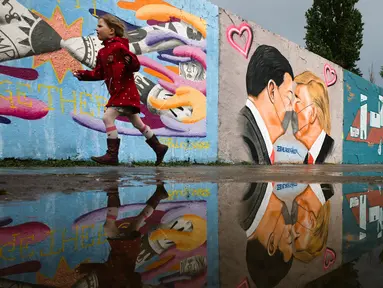 Anak-anak berlari di depan Graffiti yang menggambarkan Presiden AS Trump (kanan) dan Presiden Tiongkok Xi Jinping saling berciuman dengan mengenakan masker di tembok taman umum Mauerpark di Berlin, Jerman, Rabu, (29/4/2020). (AP/Markus Schreiber)