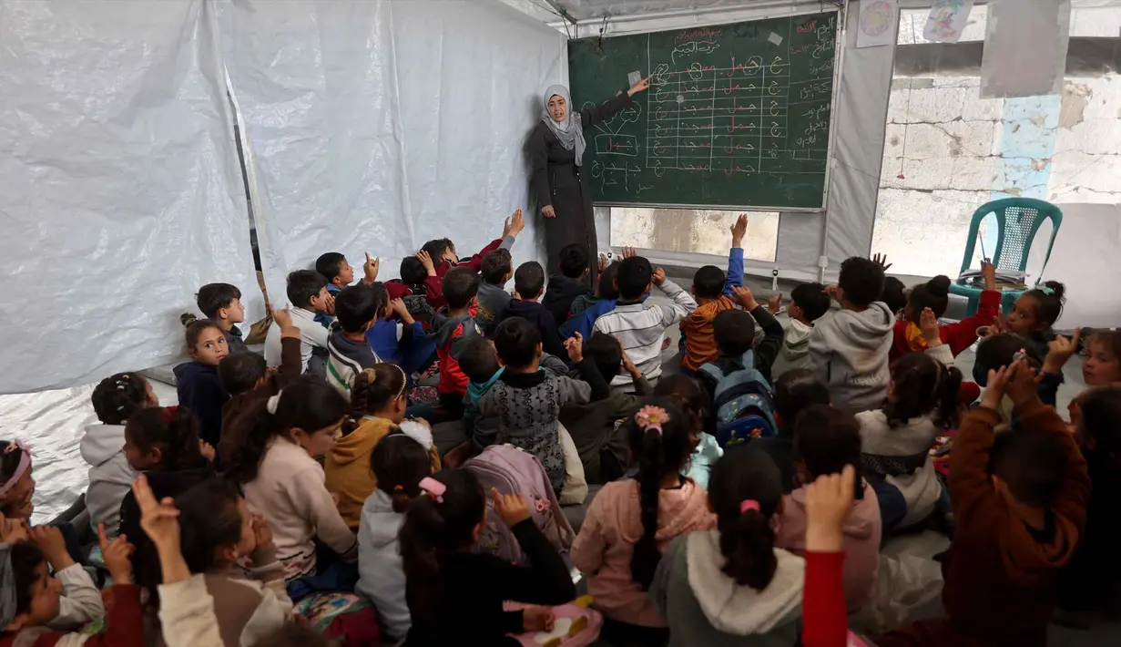 Anak-anak pengungsi Palestina mengikuti kegiatan belajar mengajar di dalam tenda di Sekolah Mada, kamp pengungsi Jabalia, Jalur Gaza Utara pada 13 April 2026. Sekolah Mada menjadi salah satu titik di mana anak-anak pengungsi Palestina tetap bisa mengikuti kegiatan belajar-mengajar. (Omar AL-QATTAA/AFP)
