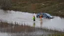 Luapan sungai Herault diperkirakan akan menyebabkan beberapa kerusakan signifikan. Tampak dalam foto, petugas penyelamat berjalan melewati sebuah mobil di sepanjang sungai Herault yang meluap setelah hujan lebat di Agde, Prancis selatan pada Selasa 23 Desember 2025. (Sylvain THOMAS/AFP)