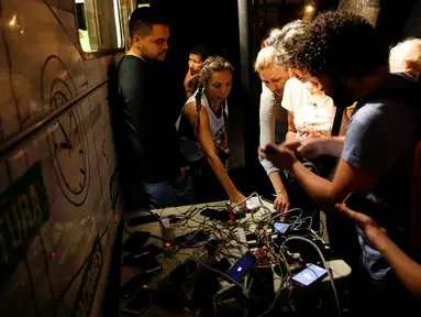 Warga nampak mengerubungi sebuah generator yang menjadi tempat pengisian baterai ponsel umum di Caracas, Venezuela (26/3). Akibat pemadaman listrik yang masih terjadi di Venezuela, warga harus mengantre dan berebut untuk mengisi daya baterai ponsel milik mereka. (Reuters/Carlos Garcia Rawlins)