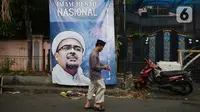 Warga berjalan di depan poster Rizieq Shihab di Jalan Petamburan 3, Jakarta, Rabu (30/12/2020). Pemerintah memutuskan untuk menghentikan kegiatan dan membubarkan organisasi massa Front Pembela Islam (FPI). (merdeka.com/Imam Buhori)
