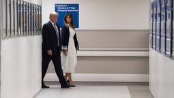 Presiden AS Donald Trump berjalan bersama istrinya di lorong rumah sakit di Florida (16/2). Trump mengunjungi rumah sakit tersebut untuk memberi penghormatan kepada korban penembakan massal yang menewaskan 17 orang. (AFP Photo/Jim Watson)
