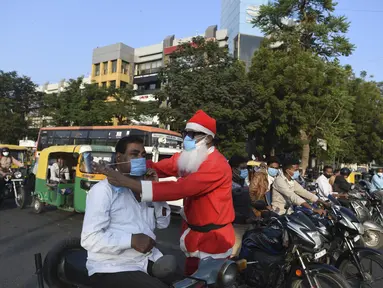 Pengguna jalan dipakaikan masker oleh presiden Angel Foundation dan pekerja sosial, Rufas Christian yang berpakaian Sinterklas di persimpangan lalu lintas di Ahmedabad, India, Kamis (17/12/2020). Aksi itu sebagai bagian dari kampanye kesadaran melawan penyebaran COVID-19. (SAM PANTHAKY/AFP)