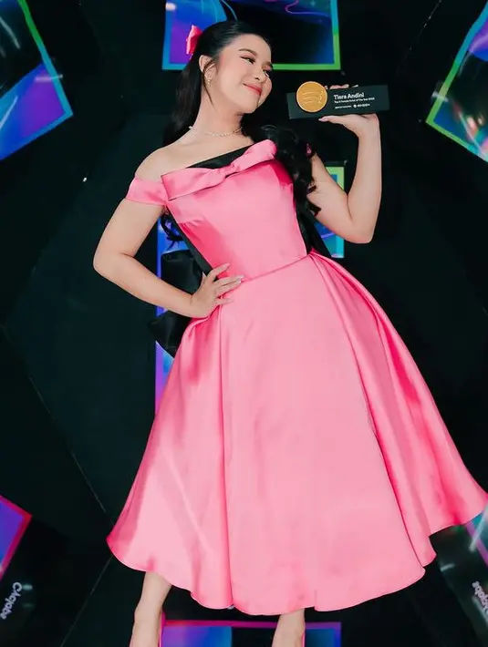 Tiara Andini tampil mengenakan dress pink one shoulder dengan aksen pita di bagian dada. Ia pun tampil dengan lerhiasan kalung dan antingnya. [@tiaraandini]