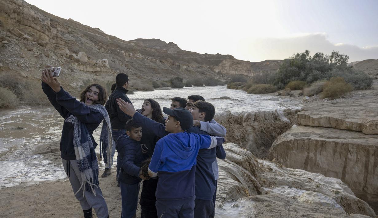 Anak-anak Israel berswafoto saat terjadi banjir bandang menyusul hujan lebat di gurun Negev di sebelah timur kota Dimona Israel pada 26 Desember 2022. Hujan lebat mengguyur Israel pada hari Senin (26/12) membanjiri jalan-jalan kota, memicu banjir bandang di dasar sungai gurun yang kering dan membasahi daerah pedesaan karena suhu turun ke level terendah musim ini. (AFP/Menahem Kahana)