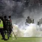 Polisi dan tentara berdiri di tengah asap gas air mata saat kerusuhan pada pertandingan sepak bola antara Arema Vs Persebaya di Stadion Kanjuruhan, Malang, Jawa Timur, 1 Oktober 2022. Ratusan orang dilaporkan meninggal dunia dalam tragedi kerusuhan tersebut. (AP Photo/Yudha Prabowo)