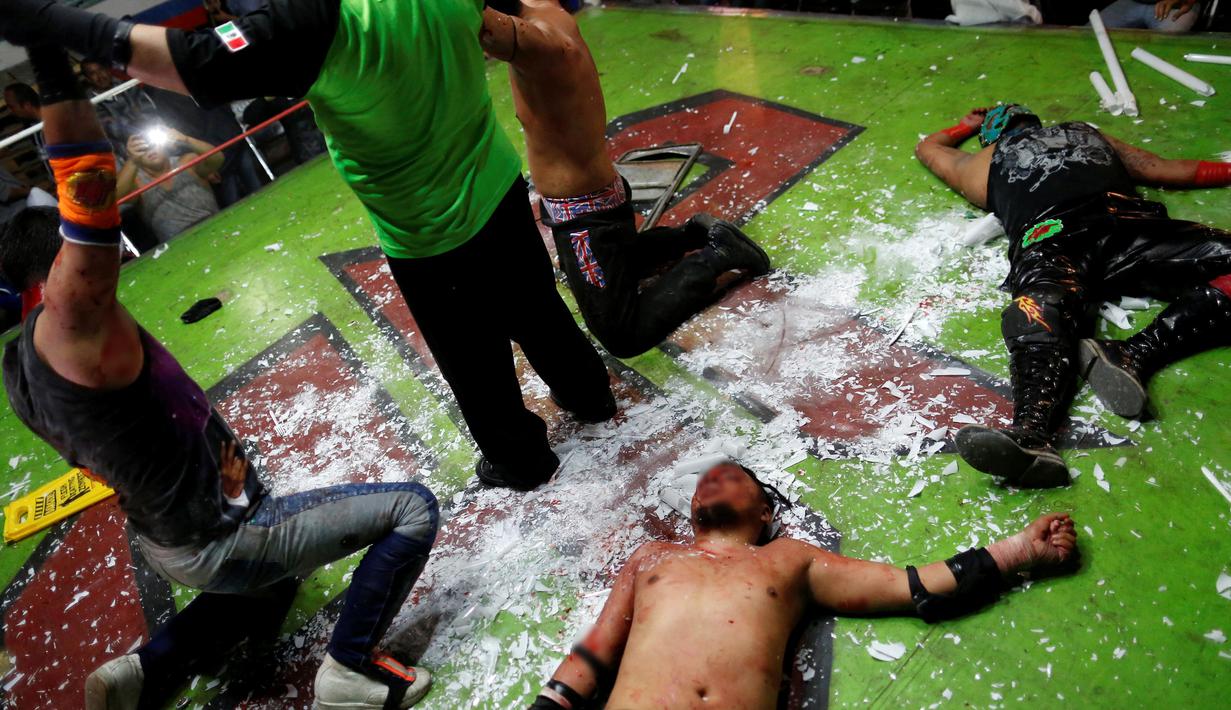 Pemain gulat yang dikenal Ciclope (tengah) terkapar di dalam ring setelah berhasil dibantai oleh lawannya, Los Malkriados dalam pertandingan gulat ekstrim di Arena Neza di pinggiran Mexico City, Meksiko (28/10). (Reuters/ Carlos Jasso)