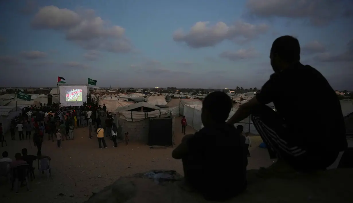 Warga Palestina menyaksikan siaran langsung pertandingan sepak bola Piala Dunia antara Spanyol dan Arab Saudi melalui layer lebar di Nuseirat, Jalur Gaza Tengah, Minggu 21 Juni 2026. (AP Photo/Abdel Kareem Hana)