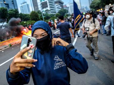 Pendemo berselfie di kobaran api saat aksi unjuk rasa di kawasan patung kuda, Jakarta, Selasa (20/10/2020). Gelombang protes tolak UU Cipta Kerja belum surut sejak disahkan pada 5 Oktober lalu. (Liputan6.com/Faizal Fanani)