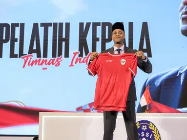 Pelatih kepala baru Timnas Indonesia, Patrick Kluivert berpose dengan memegang jersey dan memakai peci setelah sesi konferensi pers yang berlangsung di Hotel Mulia, Senayan, Jakarta, Minggu (12/01/2025). (Bola.com/Bagaskara Lazuardi)