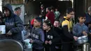 Meski perjanjian gencatan senjata antara Israel dan kelompok Hamas mengizinkan masuknya hingga 600 truk bantuan per hari, otoritas Gaza menyebut volume aktual yang diizinkan hanya sekitar 38 persen dari tingkat pasokan sebelum perang. Tampak dalam foto, anak-anak pengungsi Palestina menunggu untuk menerima makanan dari dapur amal di kamp pengungsi Nuseirat, Jalur Gaza Tengah pada 13 April 2026. (Eyad Baba/AFP)