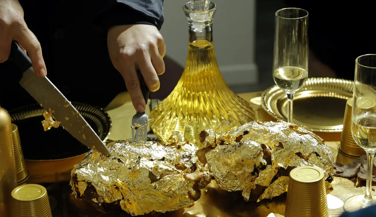 Seniman Prancis, Frederique Lecerf membungkus ayam dengan lembaran emas tipis 24 karat dalam acara makan malam di Paris, 28 Maret 2019. Tidak hanya makanan, balutan warna emas menyelimuti peralatan makan di atas meja. (REUTERS/Philippe Wojazer)