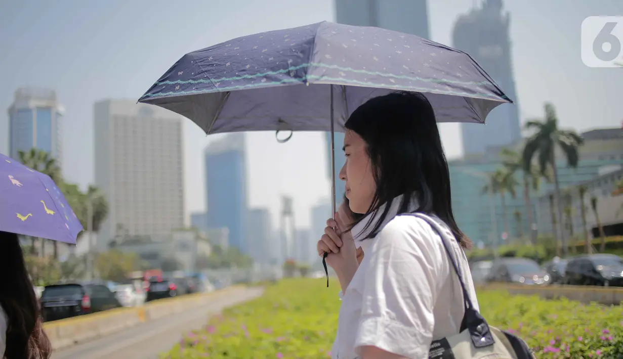 Seorang wanita menggunakan payung selama gelombang panas di Jakarta, Selasa (22/10/2019).  BMKG memprediksi wilayah Indonesia akan mengalami panas selama kurang lebih satu minggu ini. Hal ini dikarenakan matahari yang berada dekat dengan jalur khatulistiwa. (Liputan6.com/Faizal Fanani)