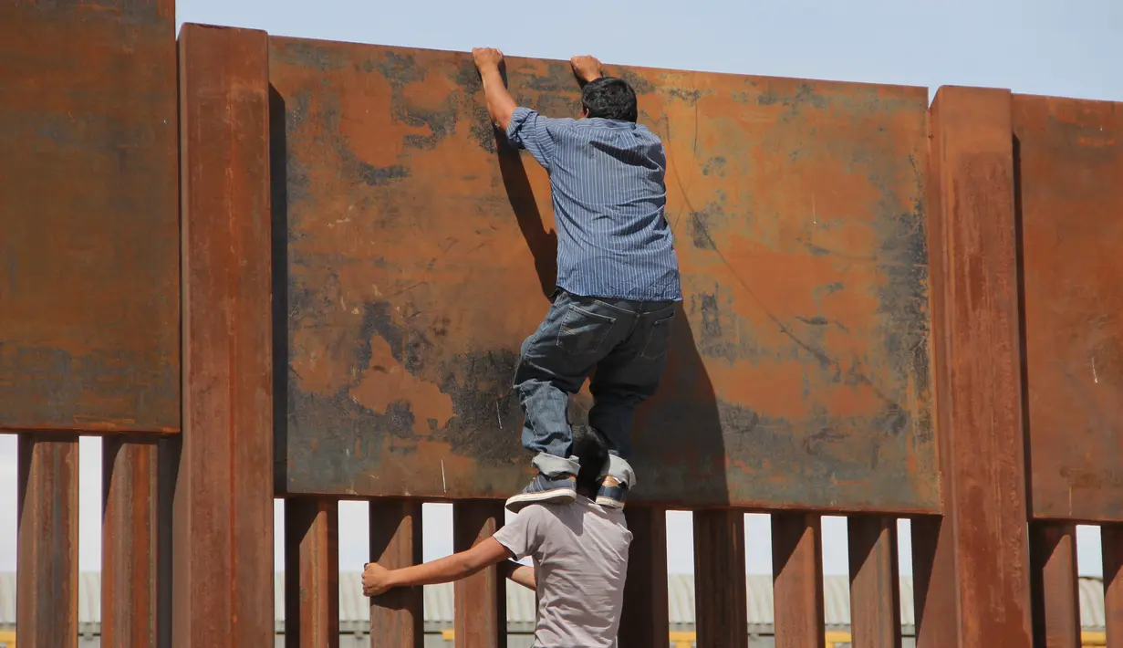 Seorang pemuda dibantu temannya memanjat tembok besi perbatasan antara Meksiko dan Amerika Serikat di negara bagian Chihuahua, Meksiko (6/4). Mereka menyeberang secara ilegal ke Sunland Park dari Ciudad Juarez. (AFP/Herika Matinez)