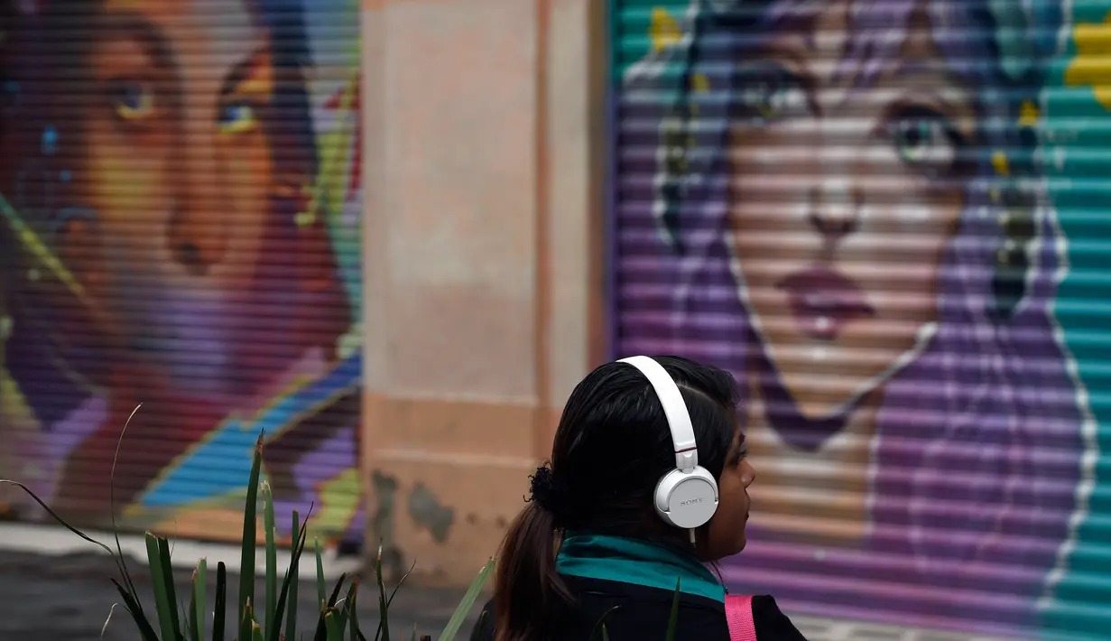 Seorang wanita duduk di depan toko yang dihiasi mural sebagai bagian dari program pemerintah di Mexico City, 30 Agustus 2017. Mural  sebagai bagian dari upaya pemerintah menghidupkan kembali ruang publik di wilayah kota tua. (ALFREDO ESTRELLA/AFP)