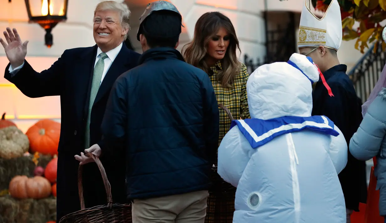 Presiden AS Donald Trump melambaikan tangan ketika dirinya dan Ibu Negara Melania Trump memberikan permen kepada anak-anak selama yang hadir acara trick-or-treat pada perayaan Halloween di Gedung Putih, Washington, Minggu (28/10). (AP/Jacquelyn Martin)