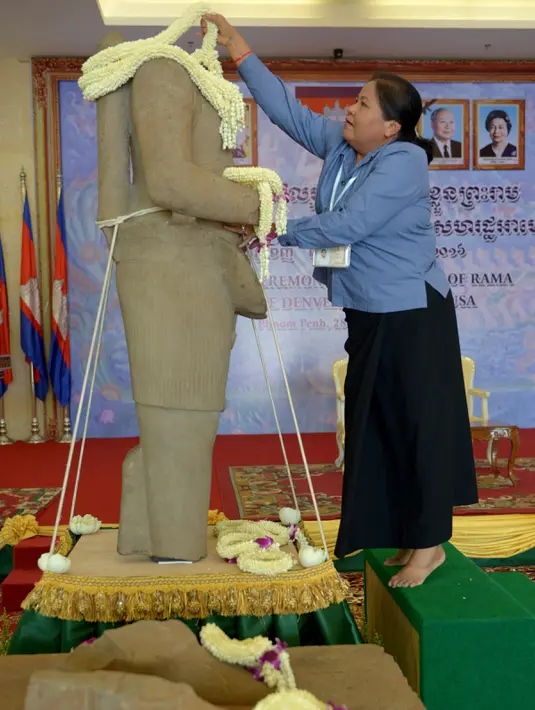 Wanita Kamboja memasangkan kalung bunga ke patung 'Tubuh Rama' dalam upacara penyerahan patung oleh Museum Seni Denver, AS, di Phnom Penh, Senin (28/3). Patung itu merupakan patung batu tak berkepala yang berasal dari Abad ke-10  (TANG CHHIN SOTHY/AFP)
