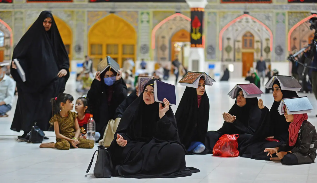 Para jemaah syiah manaruh kitab suci Al-Quran di atas kepala mereka saat menyambut malam lailatul qadar di Makam Suci Imam Ali, Najaf, Irak, Sabtu (16/5/2020). Ritual saat berdoa dan meminta hajat kepada Tuhan ini sudah berlangsung selama berabad-abad lamanya. (HAIDAR HAMDANI/AFP)