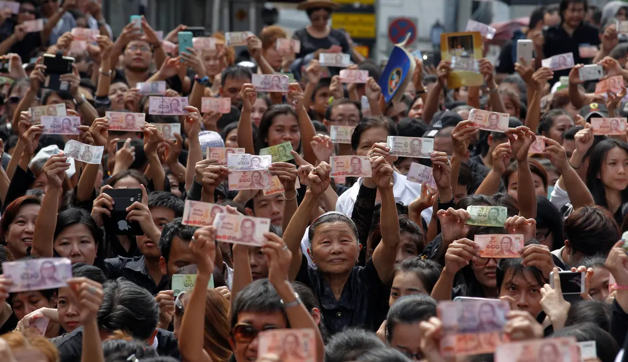 Rakyat Thailand memperlihatkan uang bergambar Raja Thailand Bhumibol Adulyadej saat menunggu pemindahan jenazah Bhumibol dari rumah sakit menuju Grand Palace, Bangkok, Thailand, Jumat (14/10). (REUTERS / Chaiwat Subprasom)