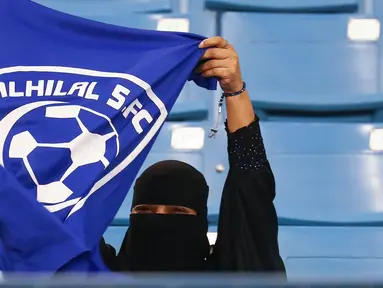 Seorang wanita mengibarkan bendera saat mendukung tim Al-Hilal dari Saudi melawan Al-Ittihad dalam pertandingan Liga Saudi Pro di King Fahd International Stadium di Riyadh (13/1). (AFP Photo/Ali Al-Arifi)