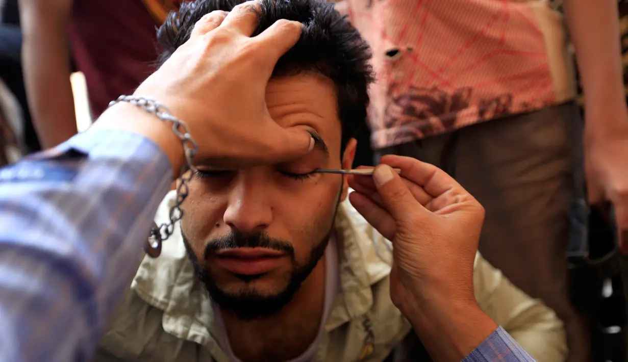 Seorang pria Yaman saat kelopak matanya dirias dengan kosmetik tradisional kohl di Masjid Agung, kota tua Sanaa pada 9 mei 2019. Bagi muslim Yaman, pemakaian kohl diyakini mampu membersihkan dan melindungi mata dari penyakit ini sudah menjadi tradisi setiap bulan Ramadan. (MOHAMMED HUWAIS/AFP)