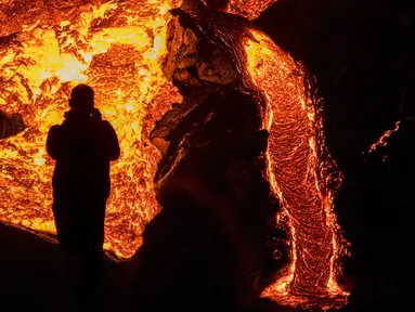 Seseorang menyaksikan aliran lahar dari letusan gunung berapi di Semenanjung Reykjanes, barat daya Islandia, Senin (29/3/2021). Letusan gunung berapi tersebut masih menarik ribuan orang yang berharap untuk mendekati aliran lahar. (AP Photo/Marco Di Marco)