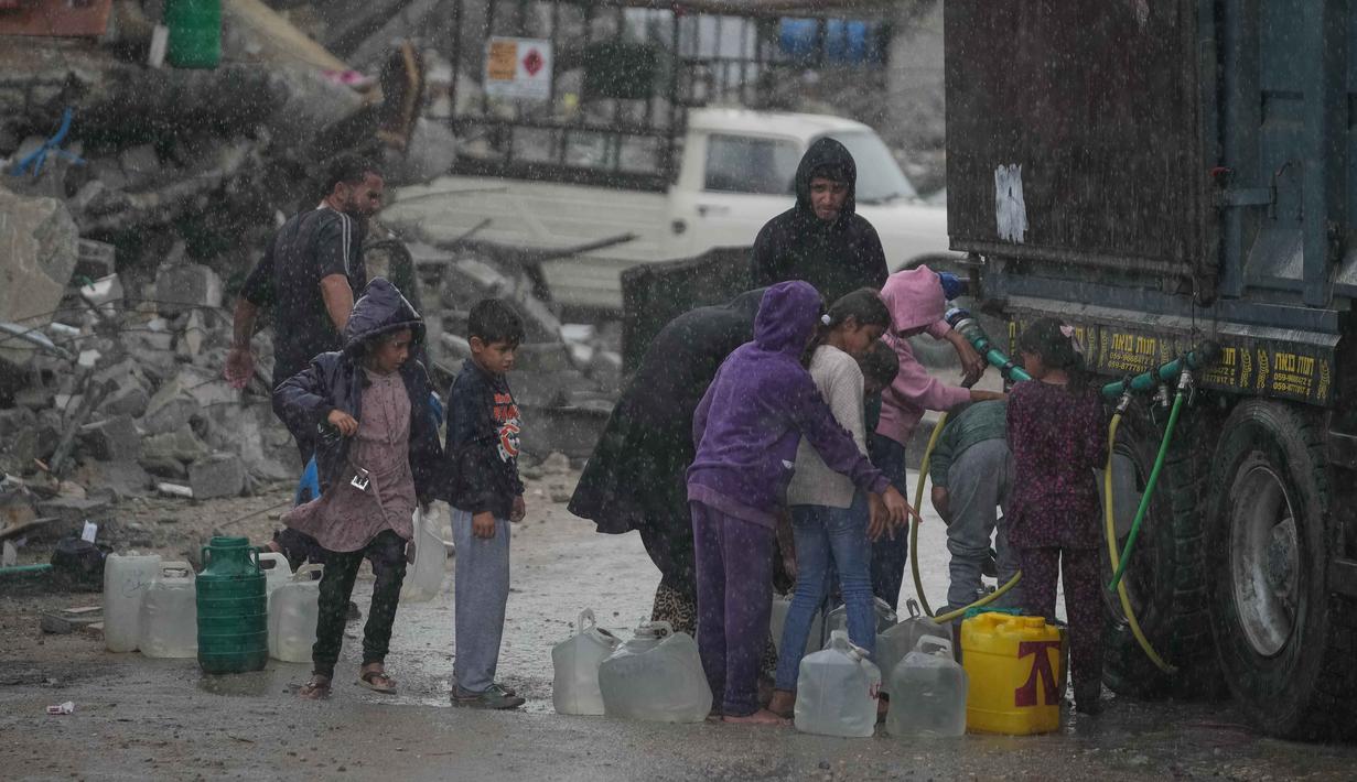 Situasi ini disebabkan kerusakan infrastruktur air dan sanitasi yang meluas, blokade bantuan kemanusiaan, dan minimnya pasokan air yang layak minum. Tampak dalam foto, anak-anak Palestina mengumpulkan air dari sebuah truk di tengah hujan deras di kawasan Sheikh Radwan, Kota Gaza, Jumat 14 November 2025. (AP Photo/Jehad Alshrafi)