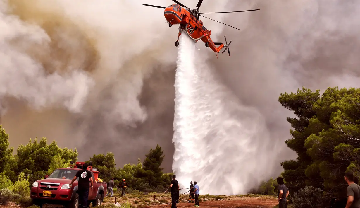 Helikopter pemadam kebakaran menjatuhkan air untuk memadamkan api saat kebakaran di Desa Kineta, dekat Athena, Rabu (24/7). Selain menewaskan puluhan orang, api juga melahap rumah, mobil, dan hutan. (AFP Photo/Valerie Gache)