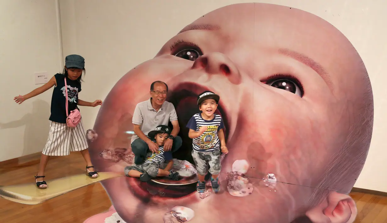 Pengunjung berpose dengan gambar 3D seorang bayi di pameran seni trik 3D karya seniman Jepang Masashi Hattori di Kawasaki, dekat Tokyo, Sabtu, (5/8). (AP Photo / Koji Sasahara)