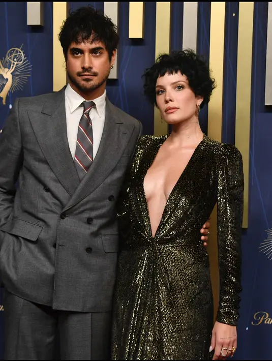 <p>Halsey dan Avan Jogia menjadi pasangan yang serasi di karpet merah Emmy Awards 2025. Halsey mengenakan Gaun lengan panjang Jean Paul Gaultier dihiasi tekstur berkilau mirip kulit ular. Bagian lehernya terbuka lebar hingga ke pusar, dengan detail ikat di pinggang yang kemudian mengalir menjadi lipit (ruched) pada kain. Sedangkan Avan dengan setelan jas abu-abu dan dasi bergaris. [Photo by Richard Shotwell/Invision/AP]</p>