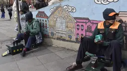 Dua tukang semir sepatu menunggu pelanggan di kawasan La Paz, Bolivia (29/11). Banyak diantara mereka masih menjalani pendidikan di sekolah dan universitas. (AFP PHOTO/Aizar Raldes)