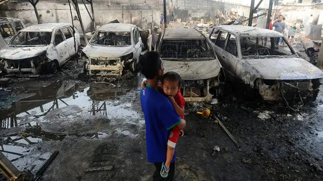 Seorang pria sambil menggendong anak melihat kondisi mobil yang hangus akibat kebakaran Depo Pertamina Plumpang (merdeka.com/Arie Basuki)