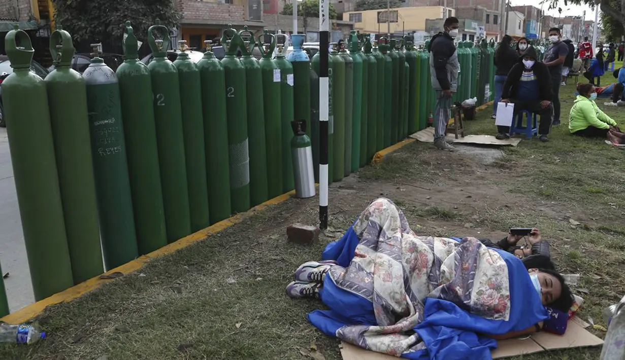 Sejumlah orang beristirahat di samping tangki oksigen kosong saat menunggu toko isi ulang buka di Callao, Peru, Senin (25/1/2021). Di tengah pandemi COVID-19, beberapa orang mengatakan mereka telah antre sehari sebelumnya untuk menjadi yang pertama saat toko buka. (AP Photo/Martin Mejia)