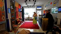 Seorang pelanggan melihat-lihat benda di The Afghan Rug Shop, Hebden Bridge, Inggris, 20 Agustus 2021. Pemilik The Afghan Rug Shop James Wilthew membeli karpet yang dicari langsung dari provinsi utara, di mana industri ini secara tradisional berbasis. (LINDSEY PARNABY/AFP)