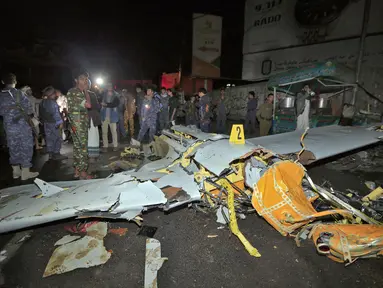 Orang-orang dan petugas keamanan berkumpul di sekitar bangkai pesawat tak berawak yang dilaporkan jatuh di ibu kota Sanaa, Yaman (23/5/2022). Pesawat tak berawak diklaim telah ditembak jatuh oleh pemberontak Houthi. (AFP/Mohammed Huwais)