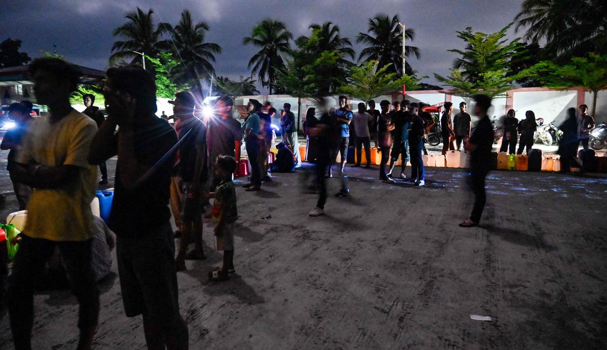 Diketahui, sejak terjadinya bencana banjir dan tanah longsor, yang diikuti dengan pemadaman listrik yang melanda sebagian besar wilayah Aceh, kebutuhan konsumsi BBM meningkat tajam. Tampak dalam foto, warga terdampak banjir mengantre untuk mendapatkan bahan bakar di sebuah Stasiun Pengisian Bahan Bakar Umum (SPBU) di Samahani, Provinsi Aceh, pada 2 Desember 2025. (CHAIDEER MAHYUDDIN/AFP)