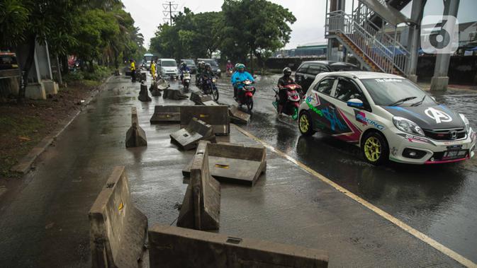 Kendaraan melintas dekat separator busway yang berserakan pascabanjir di Jalan Daan Mogot, Cengkareng, Jakarta, Jumat (3/1/2020). Separator busway tersebut berantakan akibat banjir yang menerjang sejak kemarin. (Liputan6.com/Faizal Fanani)