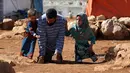 Maya Mohammad Ali Merhi (kanan) berjalan dengan sang ayah (tengah) dan seorang anak lain di sebuah kamp orang terlantar di Provinsi Idlib, Suriah, Rabu (20/6). Maya dan ayahnya lahir tanpa tubuh bagian bawah. (Aaref Watad/AFP)