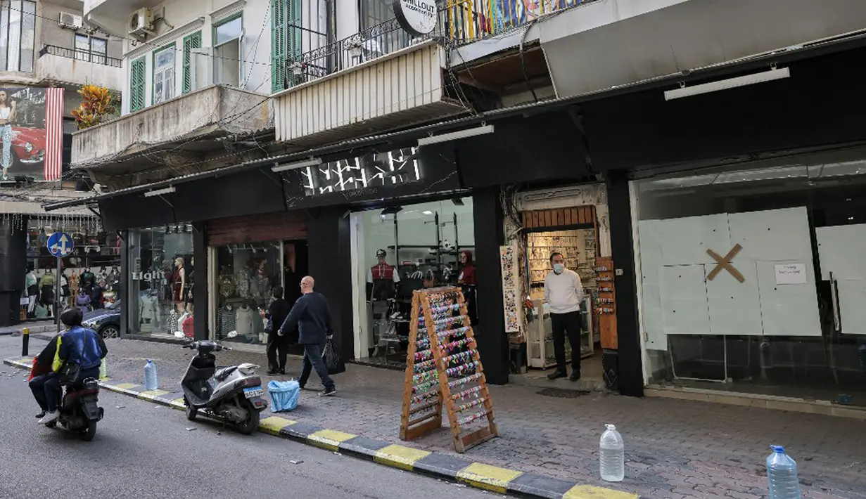 Orang-orang berjalan melewati toko-toko yang tutup atau setengah buka di kawasan Burj Hammoud, Beirut, Lebanon, 14 Desember 2021. Semarak jelang Natal yang biasa terjadi di Beirut, tak lagi terasa tahun ini karena krisis keuangan terburuk di Lebanon. (JOSEPH EID/AFP)