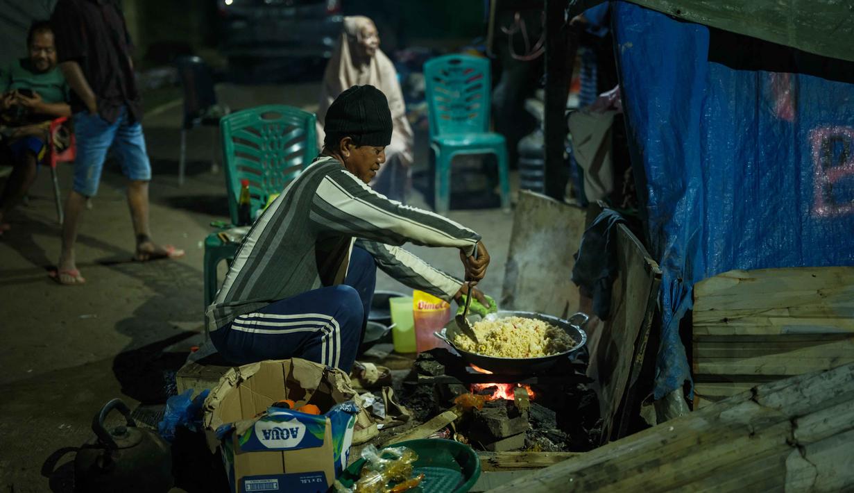 Sementara, beberapa rumah warga dan warung memakai lampu emergency maupun genset. Tampak dalam foto, seorang pria memasak untuk para pengungsi di tempat penampungan daruratnya setelah kehilangan rumahnya akibat banjir bandang di Aceh Tamiang, pada Selasa 16 Desember 2025. (Yasuyoshi Chiba/AFP)