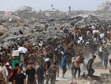 Orang-orang membawa bantuan berjalan di sepanjang jalan al-Rashid di Jabalia barat pada 22 Juni 2025, setelah truk bantuan kemanusiaan memasuki Jalur Gaza utara melalui perbatasan Zikim yang dikuasai Israel, di tengah perang yang sedang berlangsung antara Israel dan Hamas. (Omar AL-QATTAA/AFP)