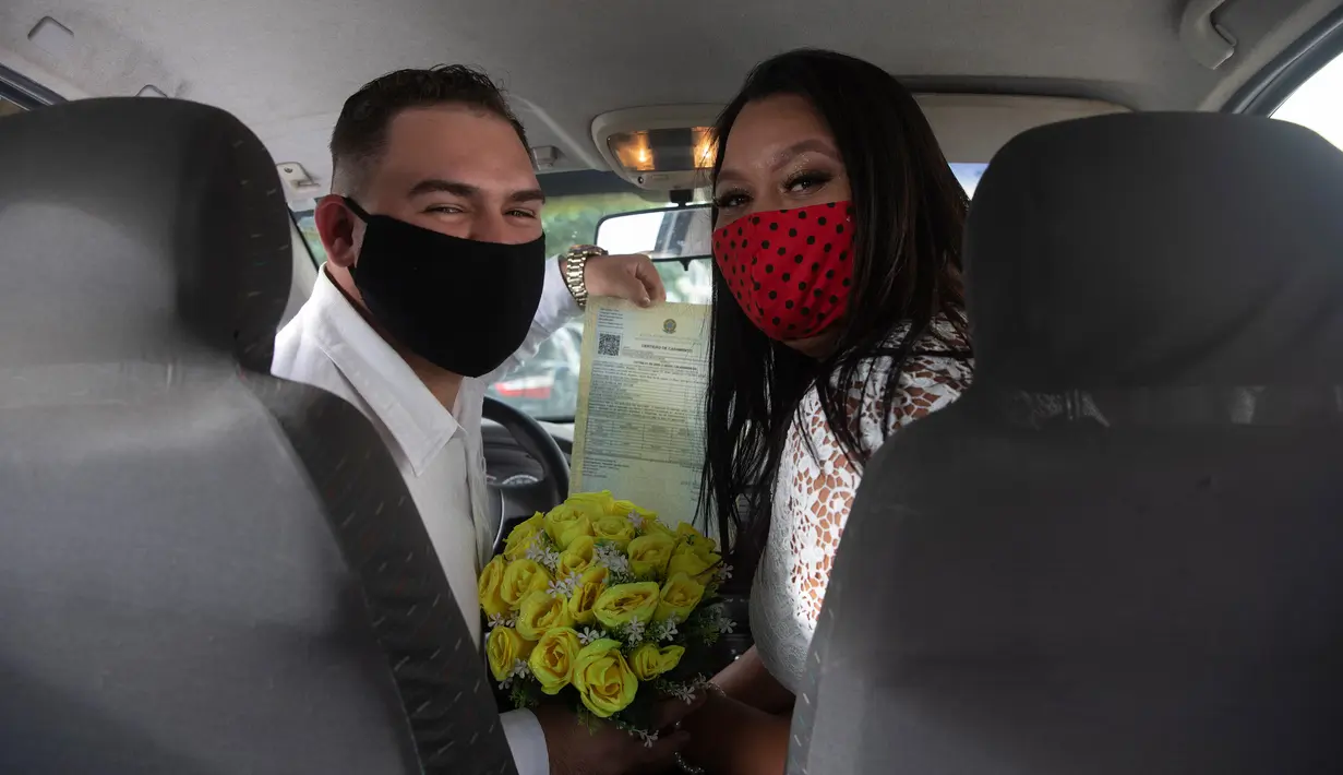 Ayrton (kiri) dan Natasha dengan mengenakan masker berpose setelah pernikahan drive-thru mereka di kantor pencatatan sipil di Santa Cruz, Rio de Janeiro, Brasil, 28 Mei 2020. Fasilitas ini untuk memudahkan pasangan yang ingin mengesahkan hubungan saat pandemi covid-19. (AP/Silvia Izquierdo)