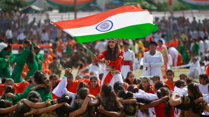 Seorang gadis mengibarkan bendera India saat para siswa melakukan tarian selama perayaan Hari Kemerdekaan India, di Jammu, India, (15/8). India merdeka dari kolonialis Inggris pada tahun 1947. (AP Photo / Channi Anand)