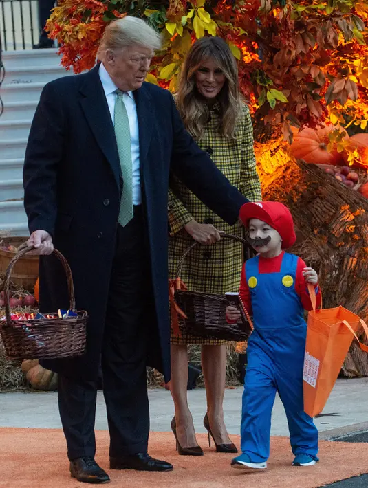 Presiden Amerika Serikat (AS) Donald Trump dan Ibu Negara Melania Trump memberikan permen kepada anak-anak selama yang hadir acara trick-or-treat pada perayaan Halloween di Gedung Putih, Washington, Minggu (28/10). (NICHOLAS KAMM / AFP)