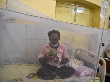 Seorang pasien minum air kelapa saat dia duduk di bawah kelambu di bangsal demam berdarah sebuah rumah sakit pemerintah di Allahabad, India (30/8/2021). (AFP/Sanjay Kanojia)