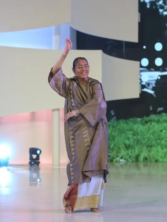 Pada pembukaan fashion Show Tangan Prive, Jajang C. Noer, menari-nari kecil mengenakan koleksi Tangan Prive. Ia tampil dengan atasan model baju kurung warna coklat dihiasi bordiran dan dipadukan kain colorful. [Adrian/Fimela]