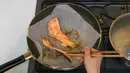 Pemenang kontes resep makanan Desa Olimpiade Tokyo 2020 Yoko Nishimura memasak sepotong salmon di Tokyo, Jepang, 12 Juli 2021. Desa Olimpiade Tokyo 2020 jadi kesempatan atlet untuk mencicipi masakan Jepang yang terkenal. (KAZUHIRO NOGI/AFP)