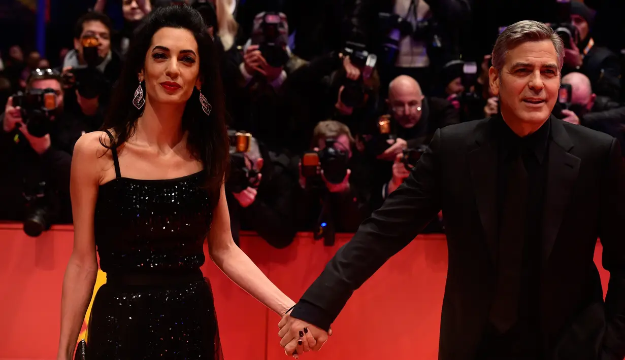 Aktor AS, George Clooney menggandeng mesra istrinya, Amal Alamuddin, saat tiba di karpet merah pemutaran film "Hail, Caesar!" pada pembukaan Berlin International Film Festival ke-66 di Berlin, Jerman, Kamis (11/2). (John MACDOUGALL/AFP)